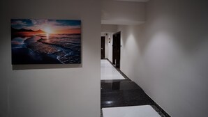 A hallway with a large painting of a sunset over water, a polished black floor, and white walls. - Sunbright Rooms Residency Hotel  (Thane)
