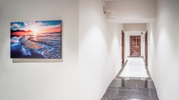 A hallway with a polished marble floor, a framed picture of a sunset over water, and a wooden door at the end. - Sunbright Rooms Residency Hotel  (Thane)