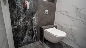 A modern bathroom with a marble shower wall, a toilet, and a small shelf with a cup. - Sunbright Rooms Residency Hotel  (Thane)