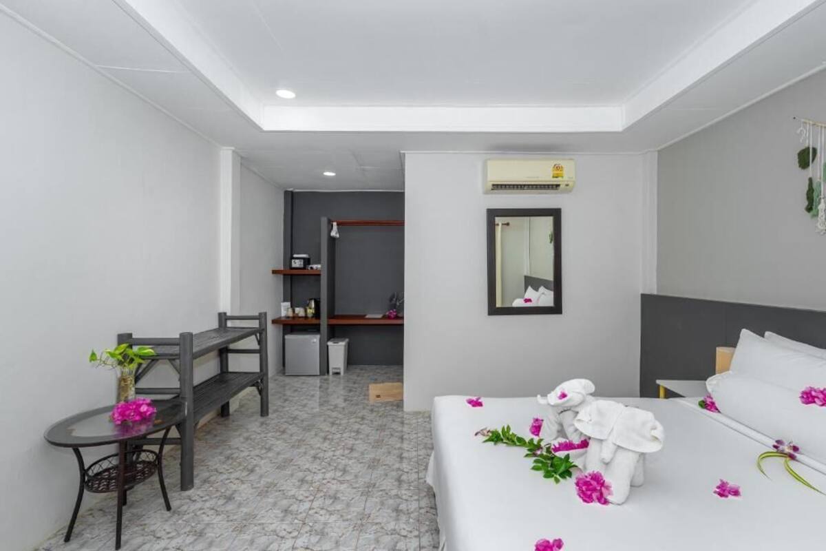 A hotel room with a bed, a desk, and a chair. There is a mirror on the wall and an air conditioning unit above it.