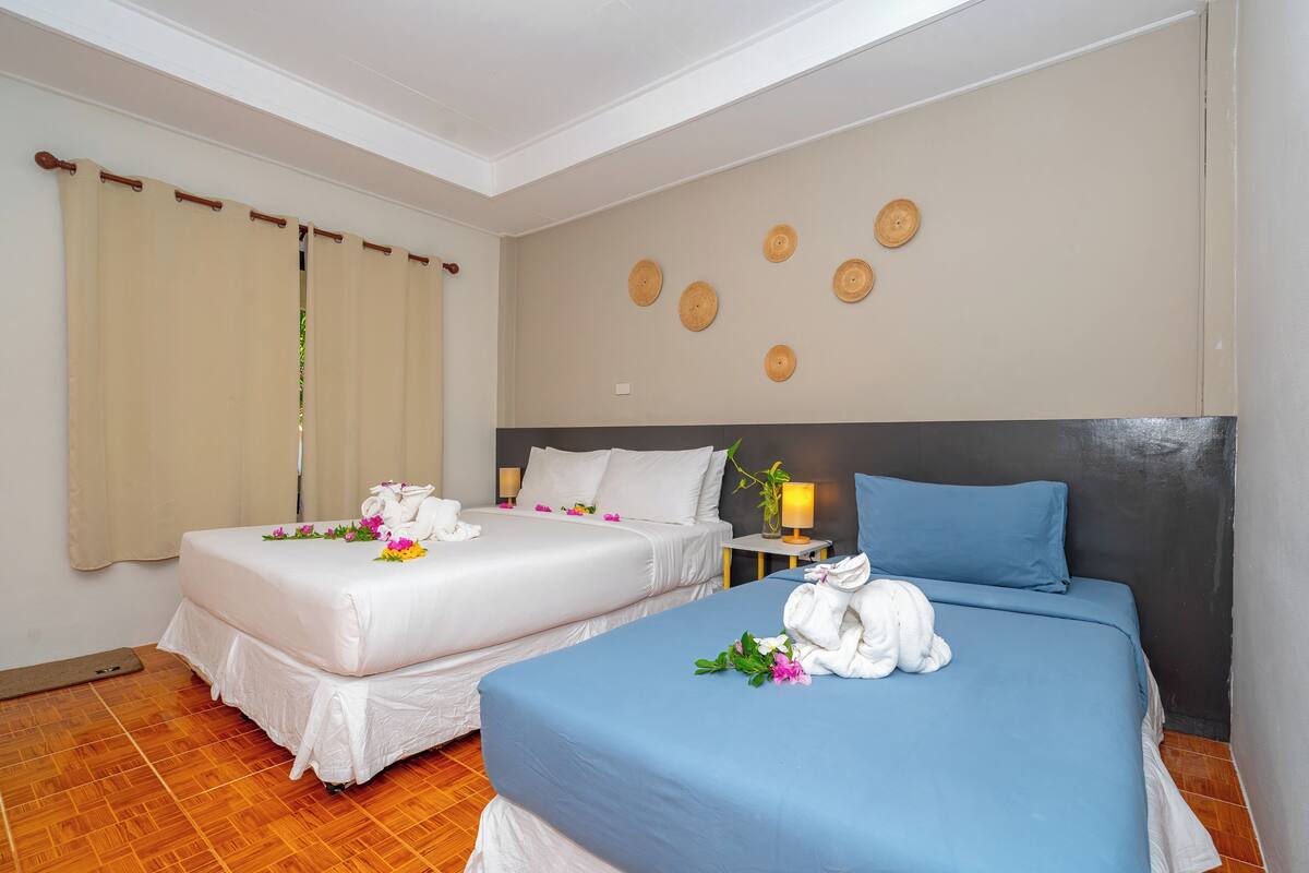 A hotel room with two beds, a wooden floor, a wall with circular decorations, and a nightstand with a lamp.