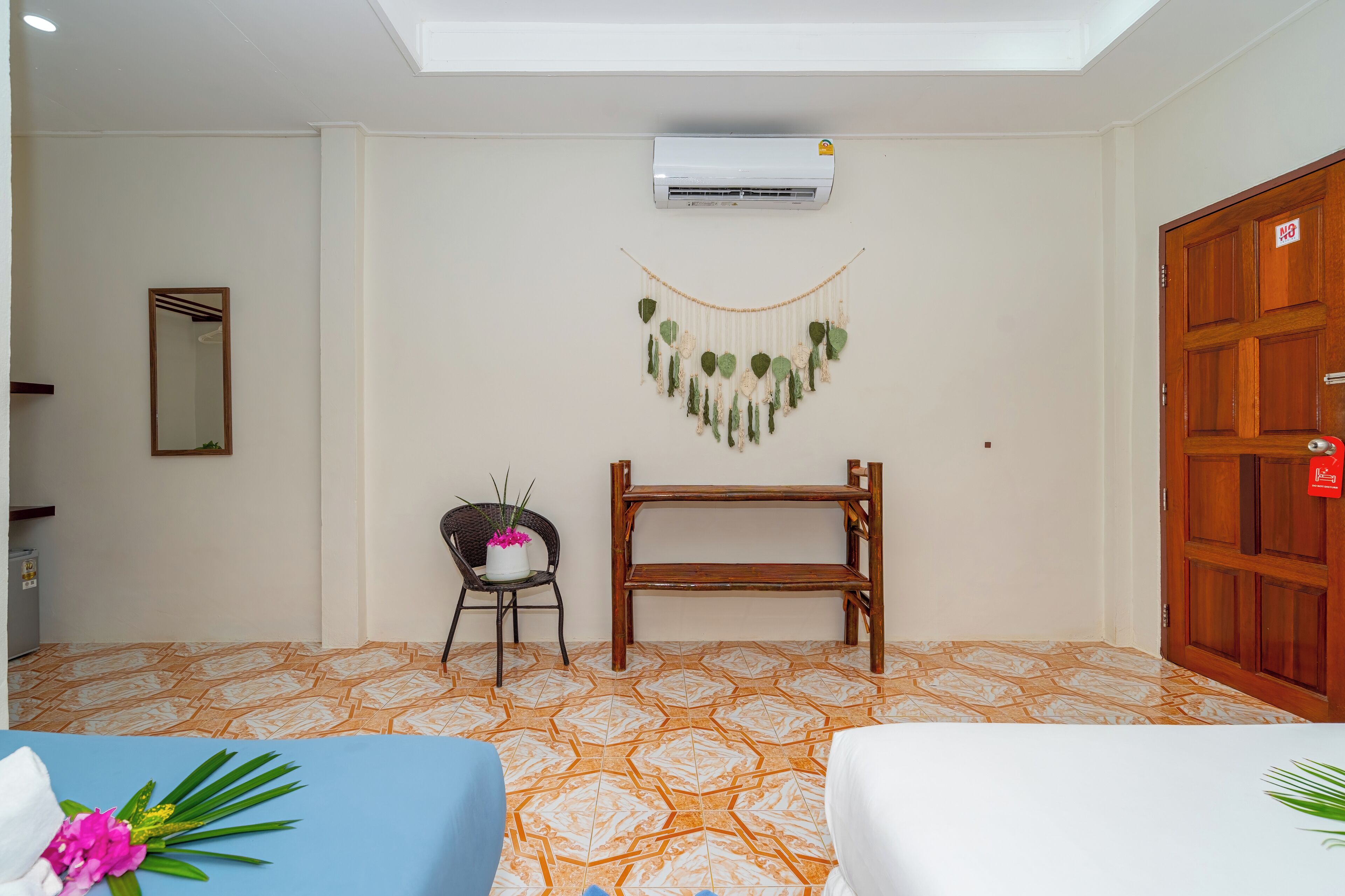 Habitación de hotel con suelo estampado, un banco de madera, una silla con planta en maceta, aire acondicionado montado en la pared y una puerta de madera con un letrero rojo.