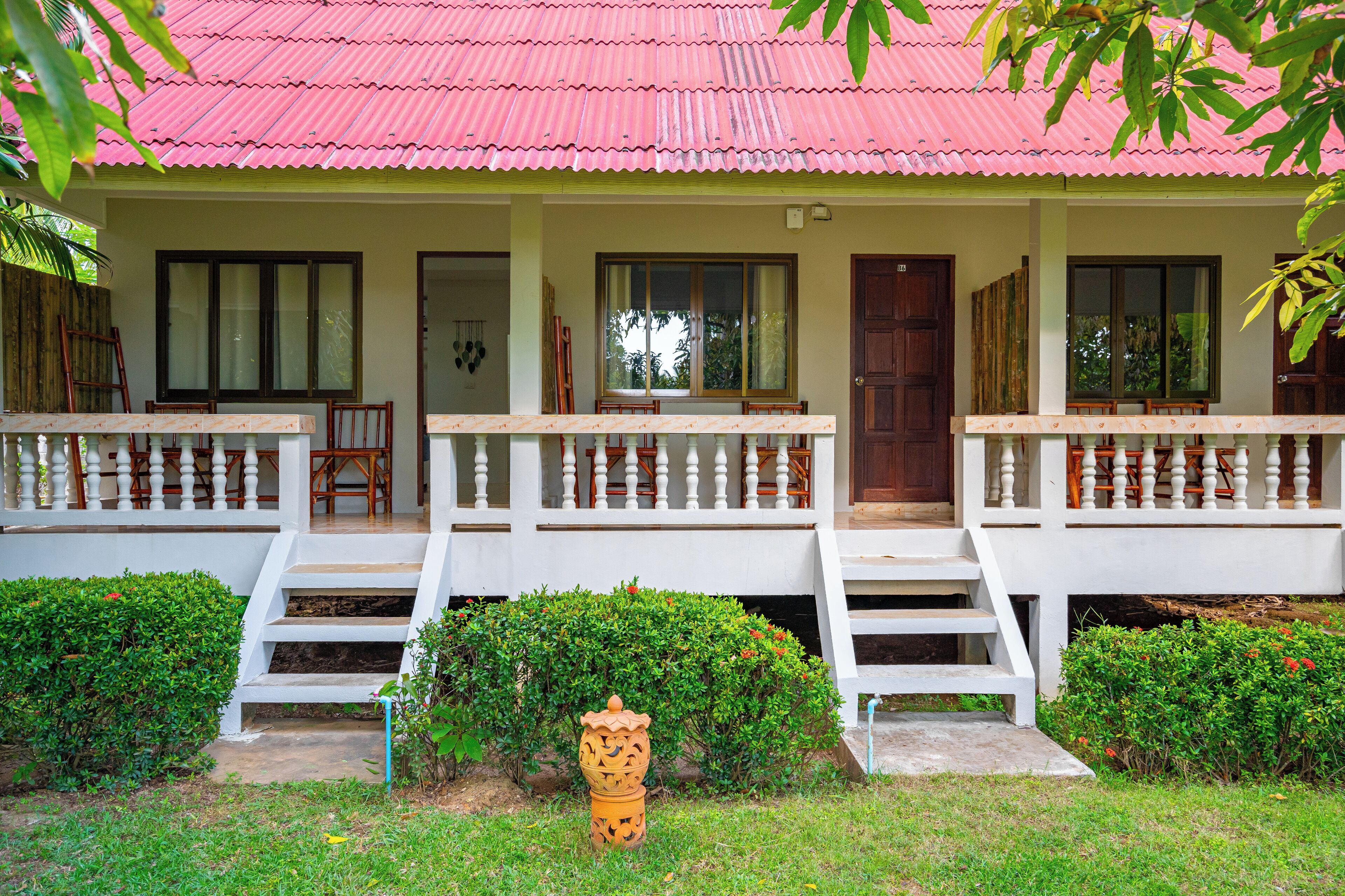 A two-story house with a red roof, white exterior, and a small front porch with steps leading to the entrance.