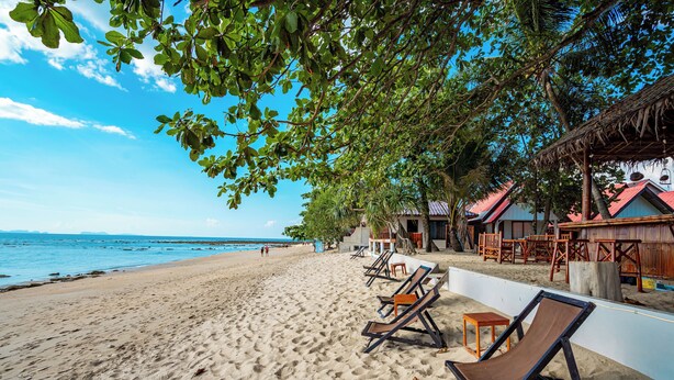 Una spiaggia con lettini, una capanna di legno e un cielo azzurro limpido.