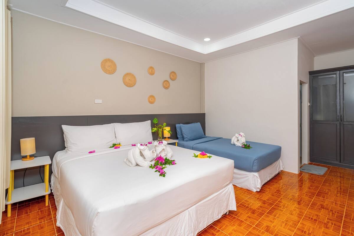 A hotel room with a large bed, a smaller bed, a wardrobe, and a bedside table with a lamp.