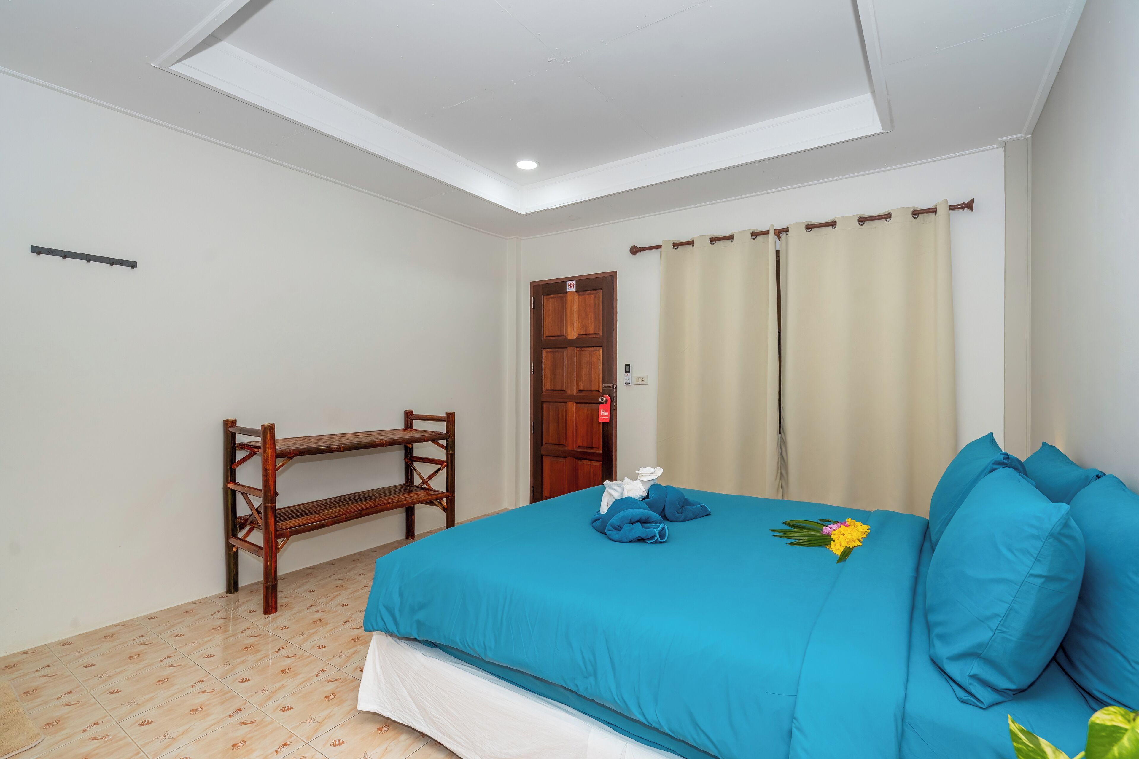 Ein Hotelzimmer mit einem Bett, einer Holzbank, einer Tür und einem Vorhang.