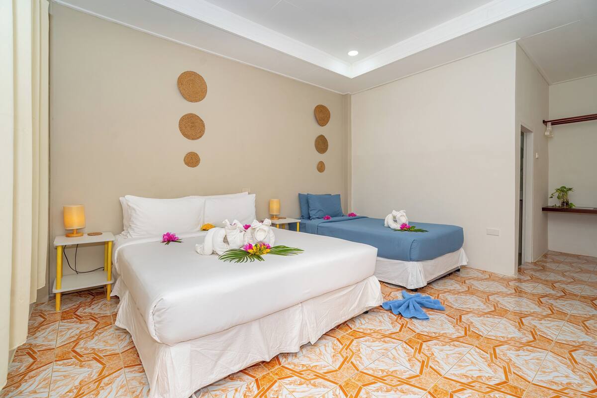 A hotel room with two beds, a small table with a lamp, and a decorative wall with circular patterns.