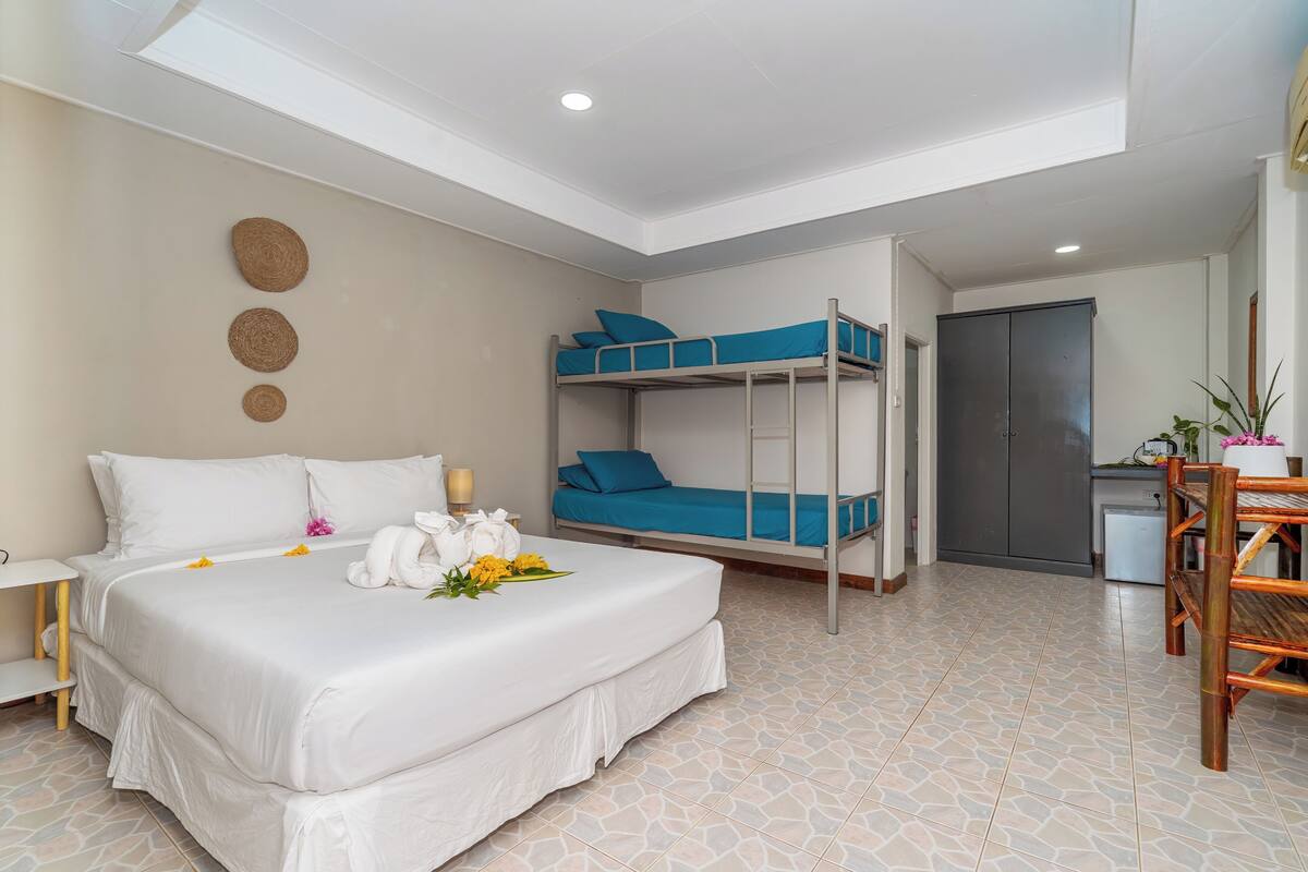 A hotel room with a large bed, a bunk bed, a desk, and a wardrobe.