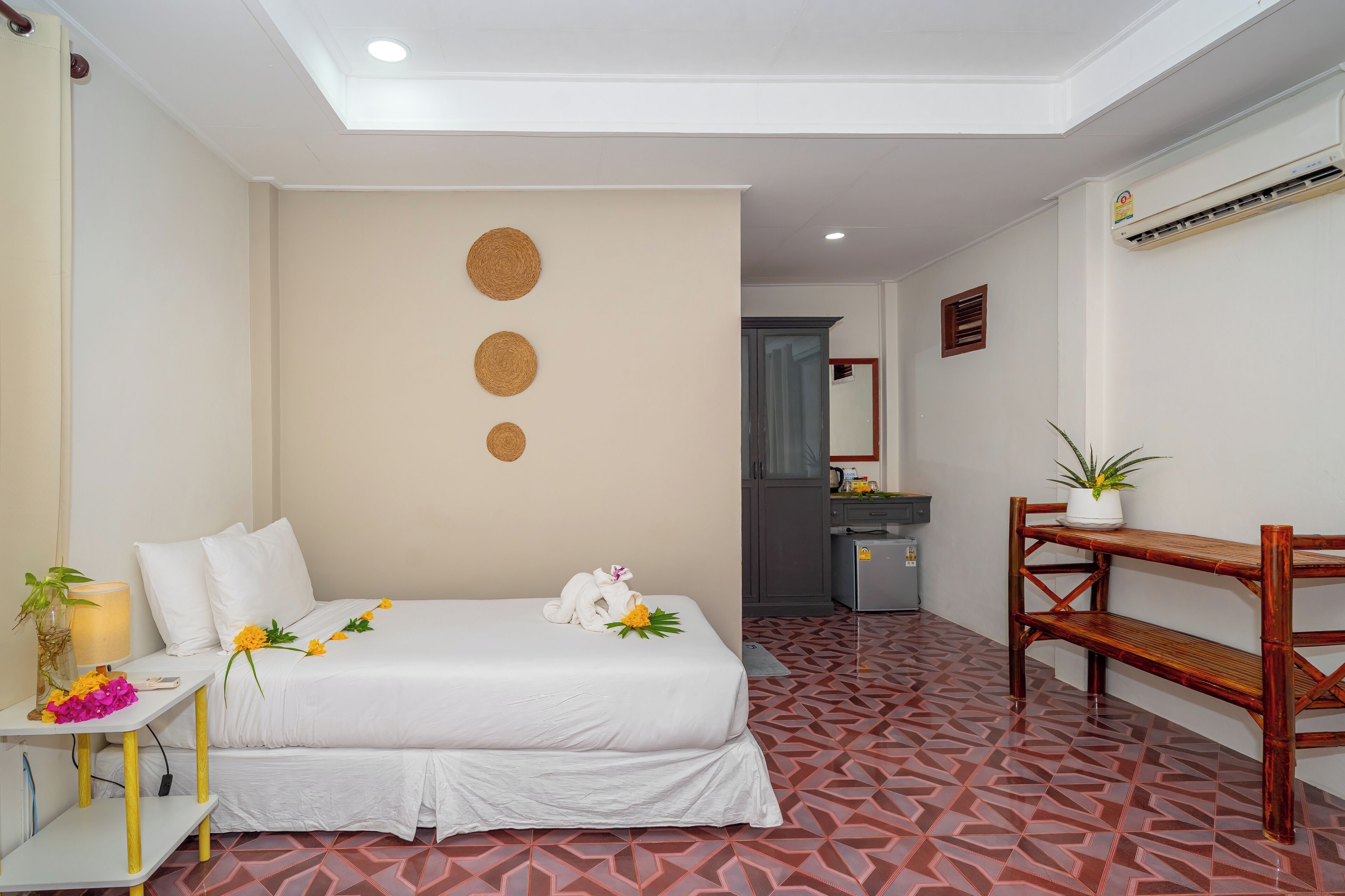 Habitación de hotel con cama, escritorio, silla, una mesita con una planta y un espejo en la pared.