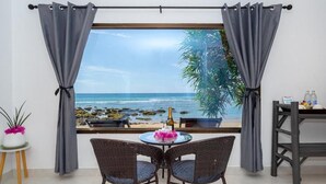 Una stanza con vista sulla spiaggia, un tavolo con sedie, una bottiglia di champagne e un cartello alla finestra.