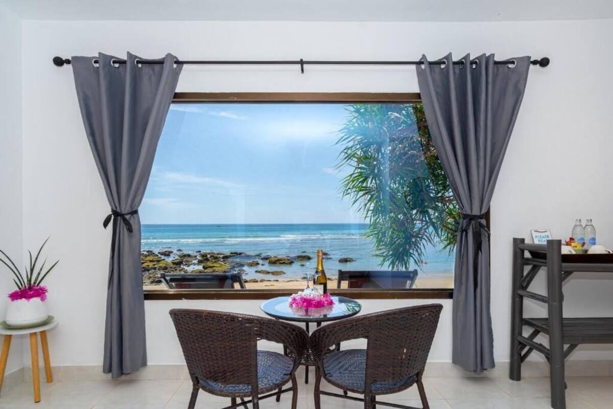 A room with a view of the beach, a table with chairs, a bottle of champagne, and a sign on the window.