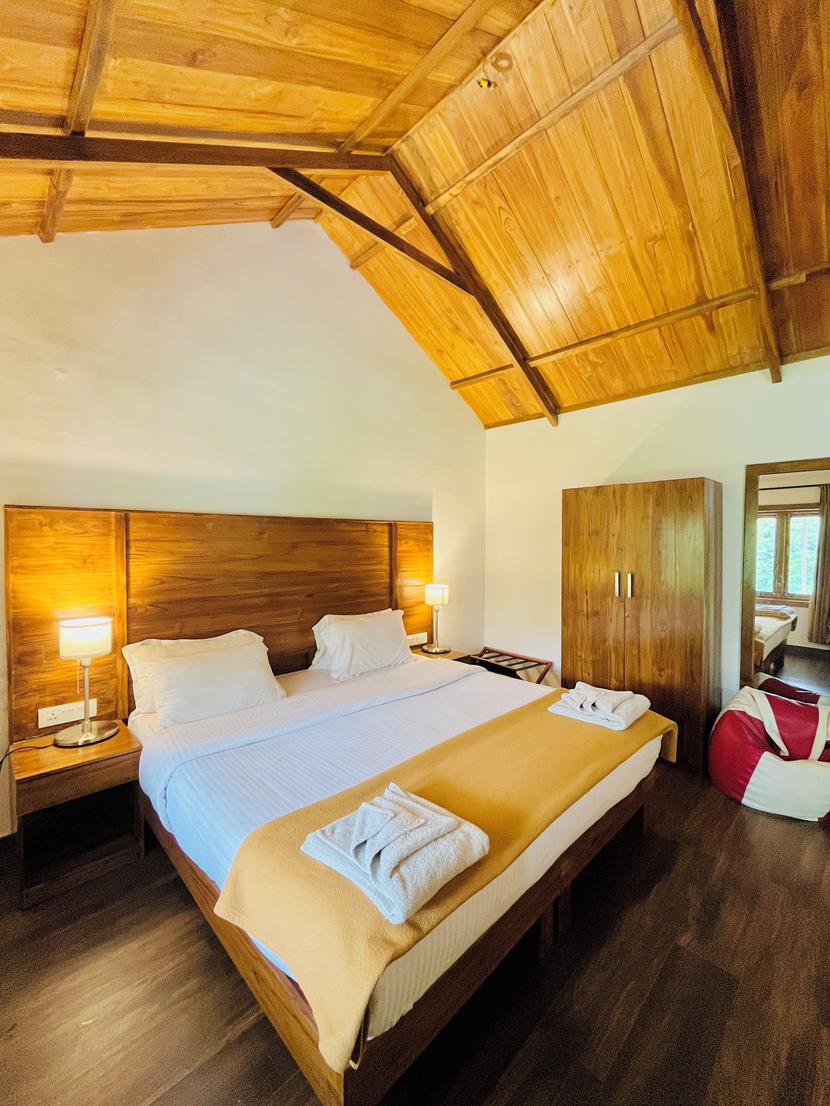 A wooden-framed bedroom with a large bed, two bedside lamps, a wardrobe, and a mirror.