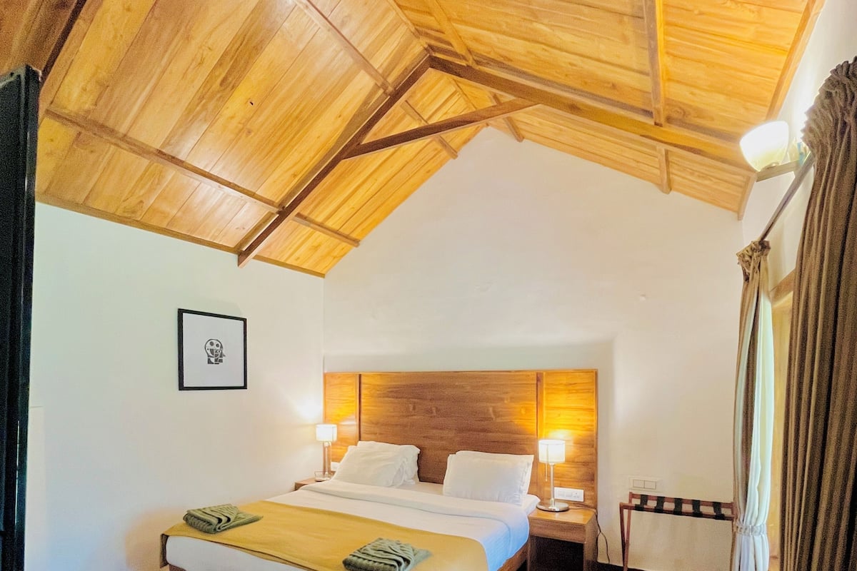 A room with a wooden ceiling, a bed with white linens, a bedside table, and a nightstand.