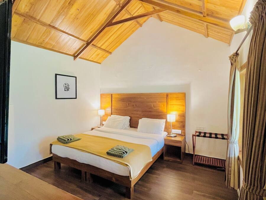 A room with a wooden ceiling, a bed with white linens, a bedside table, and a nightstand.