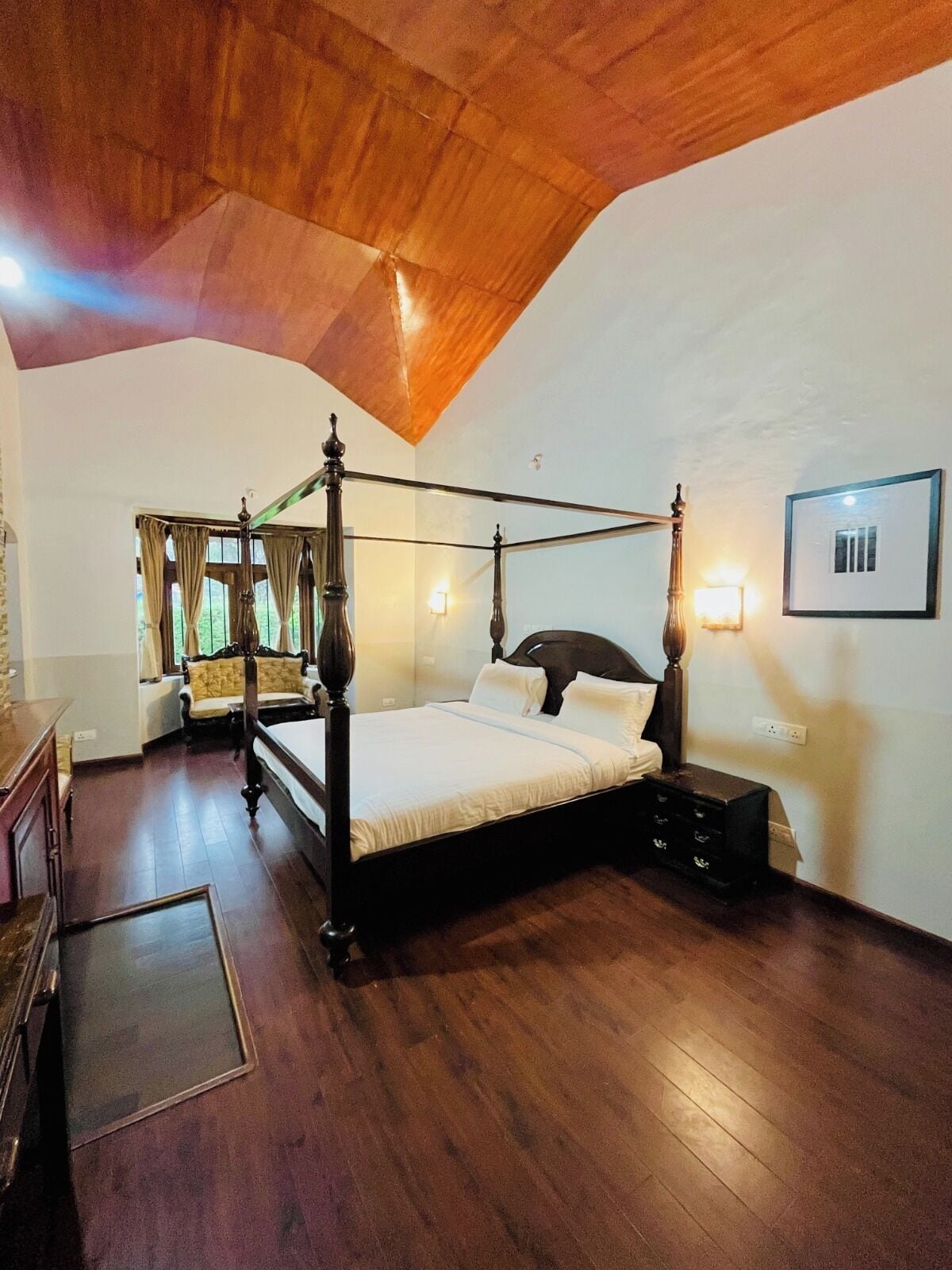 A four-poster bed in a room with wooden flooring and a sloped ceiling.