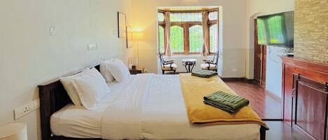 A hotel room with a wooden ceiling, a bed, a desk, a TV, and a window with curtains.