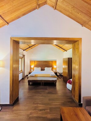 A bedroom with a wooden ceiling, a large bed, bedside lamps, and a view through an open doorway. - BouganVilla (Ootacamund)