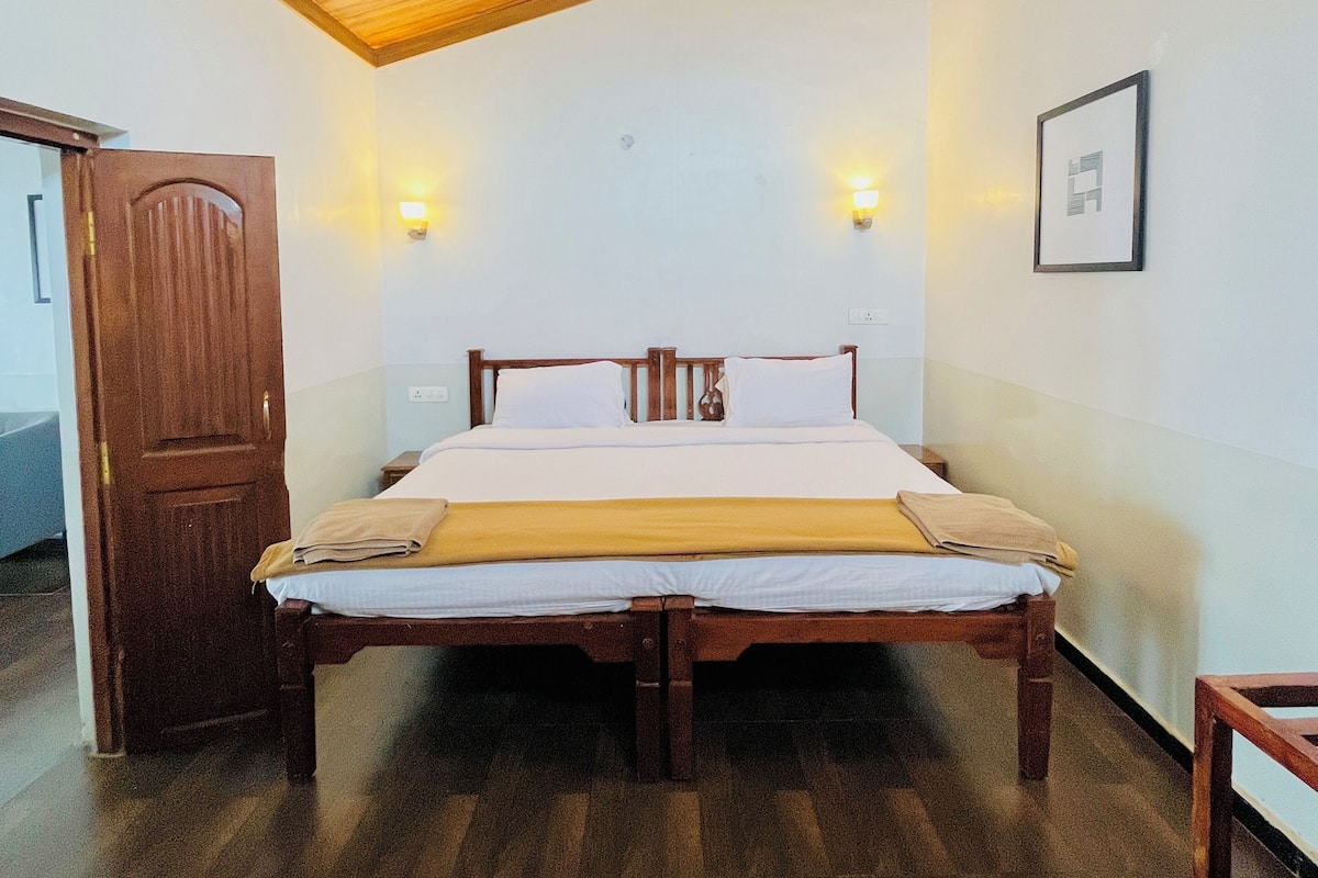 A room with a wooden ceiling, a bed with white bedding, two wall-mounted lights, and a framed picture on the wall.