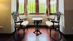 A room with a bay window, two chairs, a small table, and a light fixture. - BouganVilla (Ootacamund)