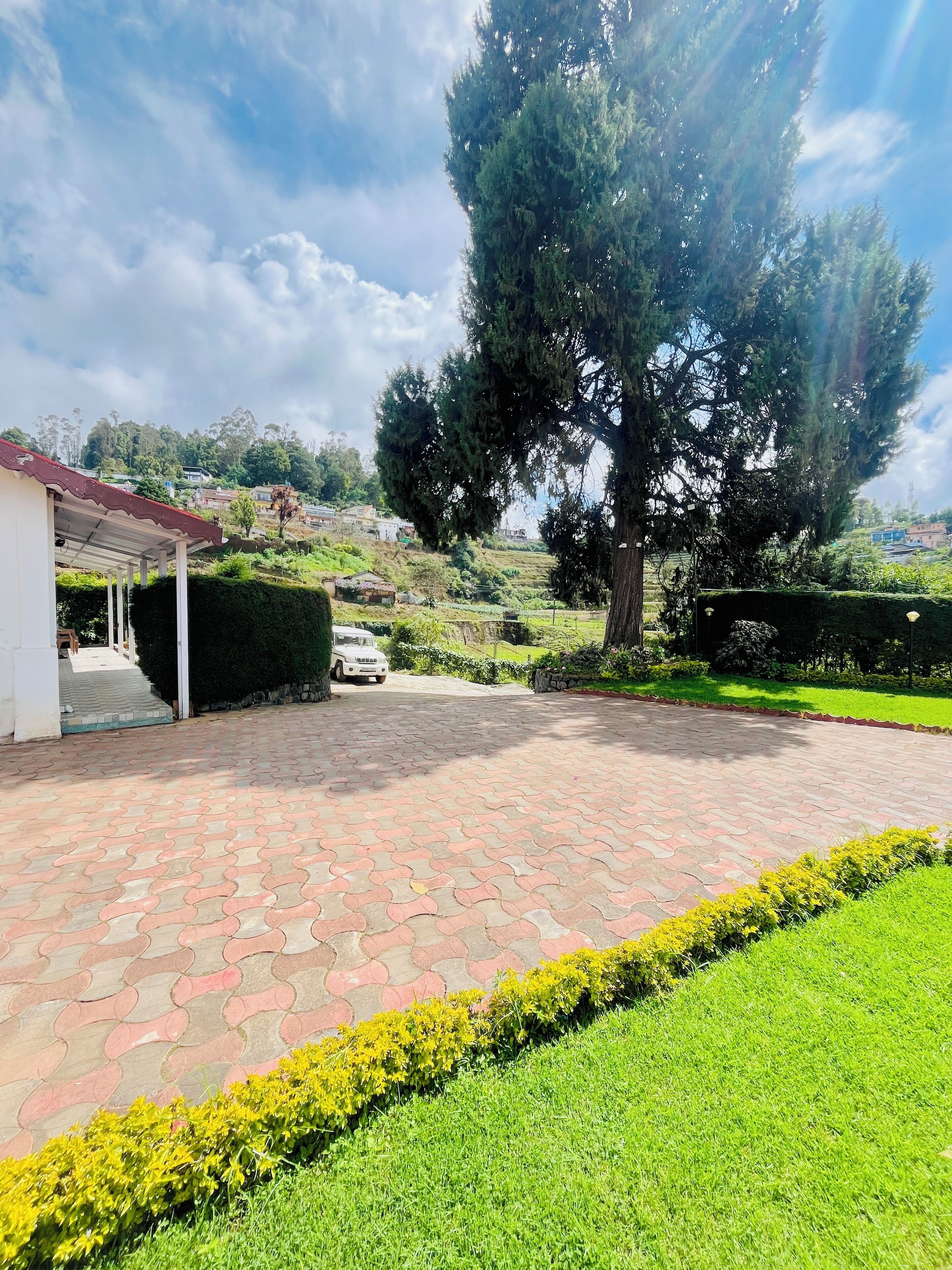 A paved driveway leading to a white building with a red roof, surrounded by well-maintained grass and a large tree.