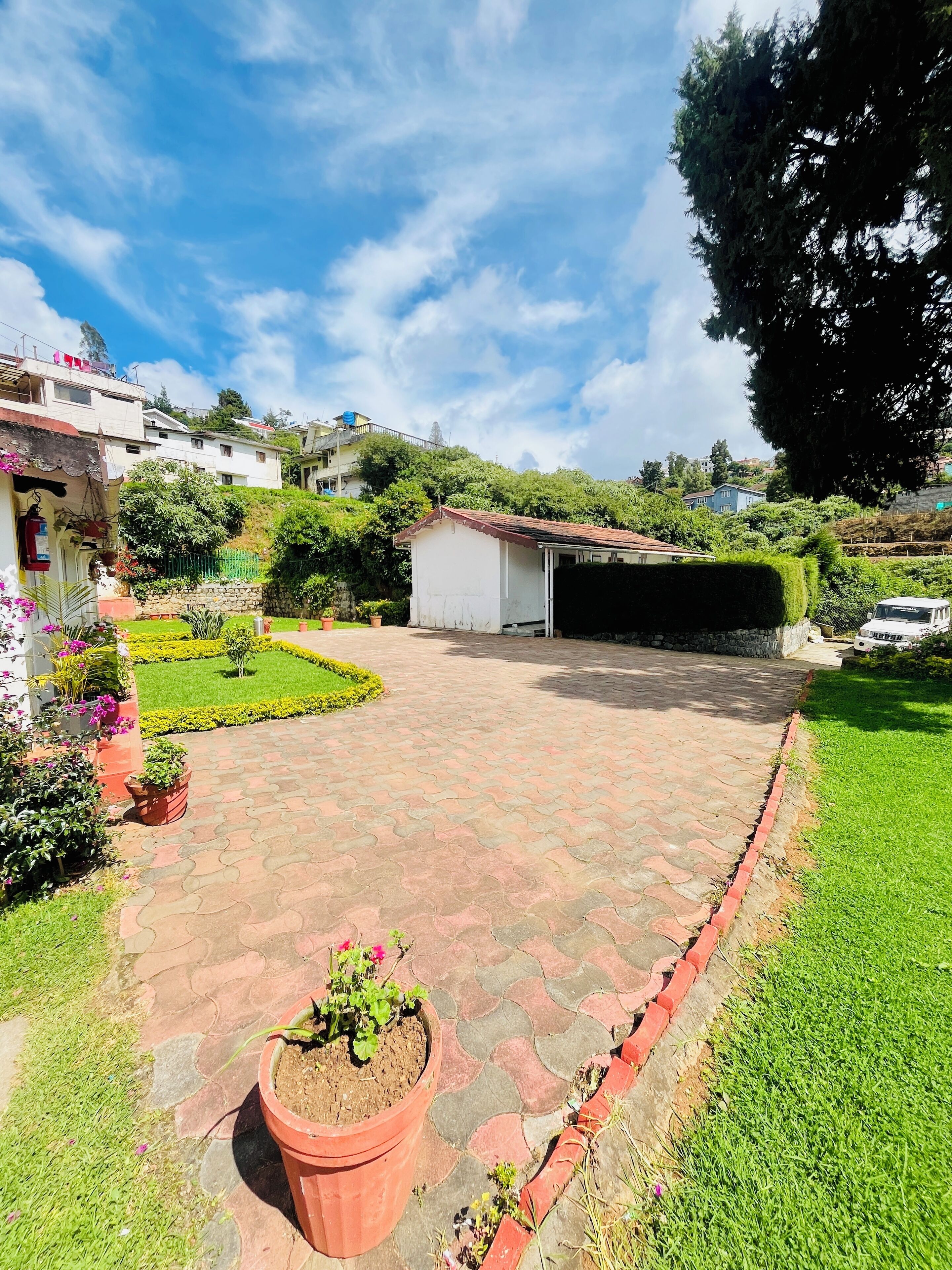 A paved courtyard with a small shed, surrounded by well-maintained lawns and potted plants.