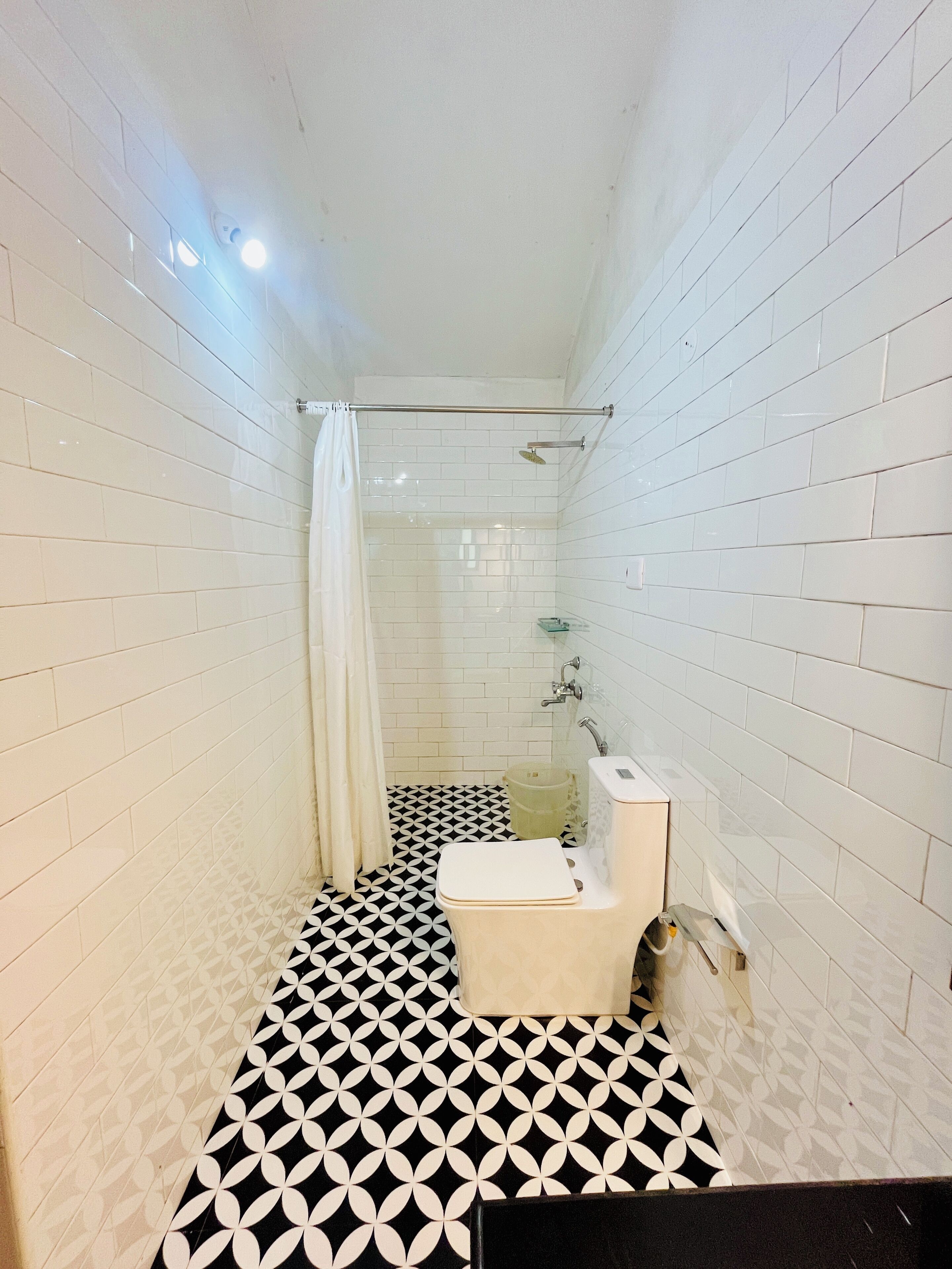 A bathroom with white tiled walls, a black and white patterned floor, a toilet, and a shower area.