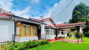 A traditional house with a red-tiled roof, a well-maintained lawn, and a clear sky. - BouganVilla (Ootacamund)