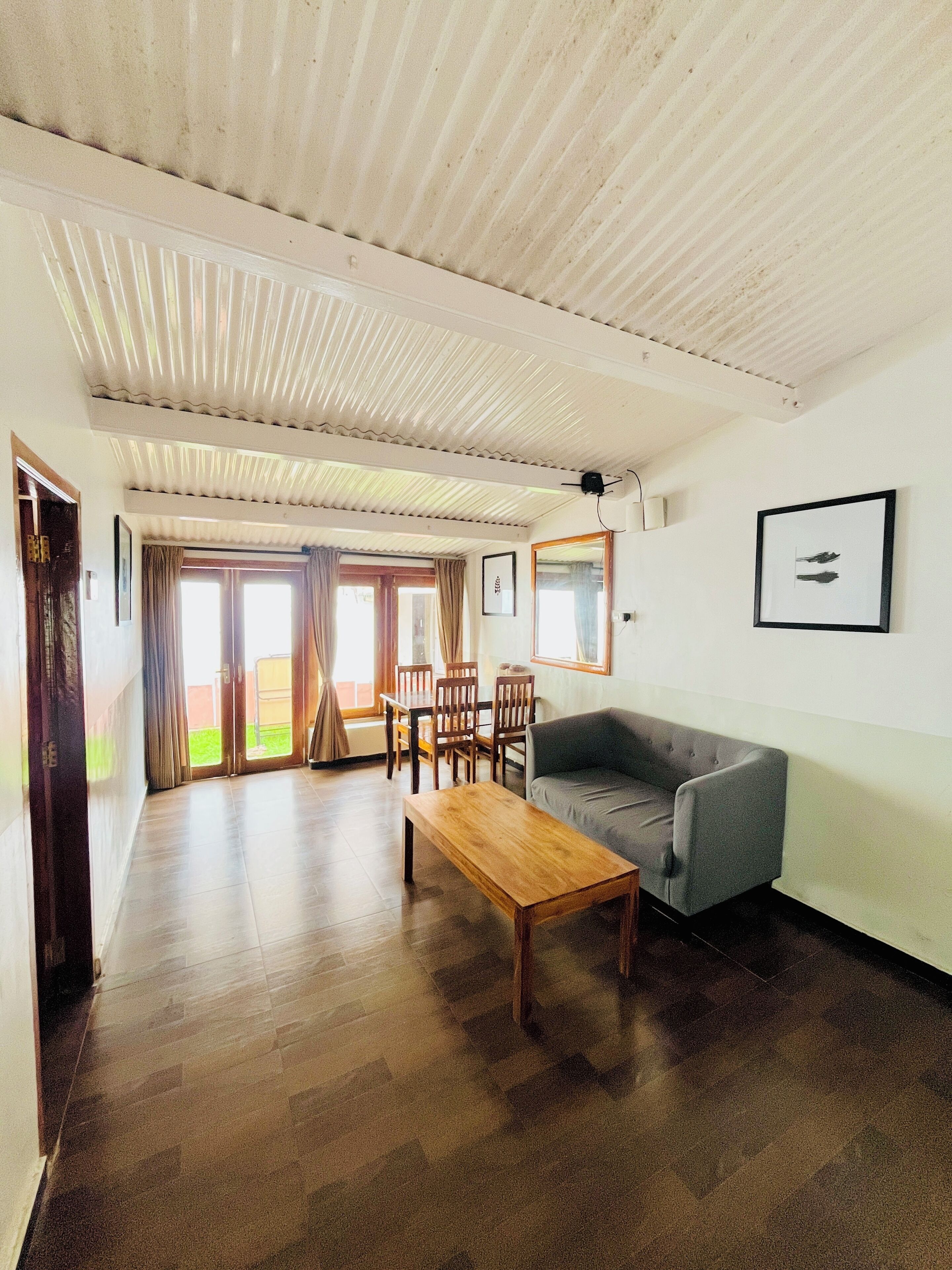 A spacious living area with a wooden coffee table, grey sofa, and a dining table with chairs.