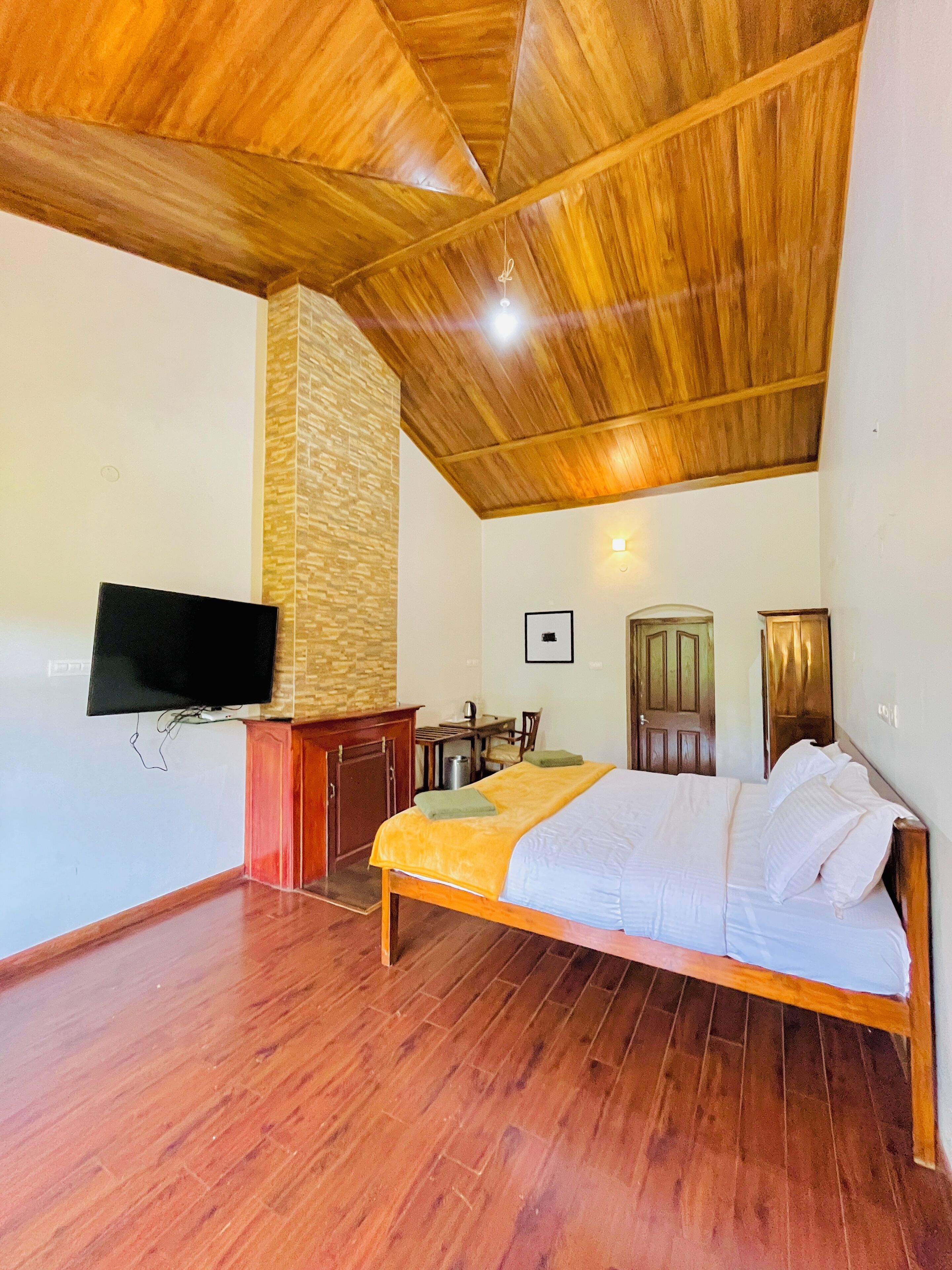Un dormitorio con techo de madera, una cama, un televisor montado en la pared, un escritorio y una silla.
