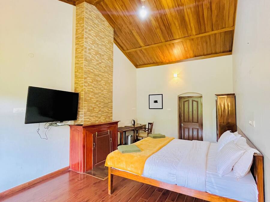Un dormitorio con techo de madera, una cama, un televisor montado en la pared, un escritorio y una silla.
