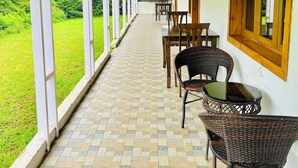 A covered corridor with a tiled floor, wooden-framed windows, and wicker furniture. - BouganVilla (Ootacamund)