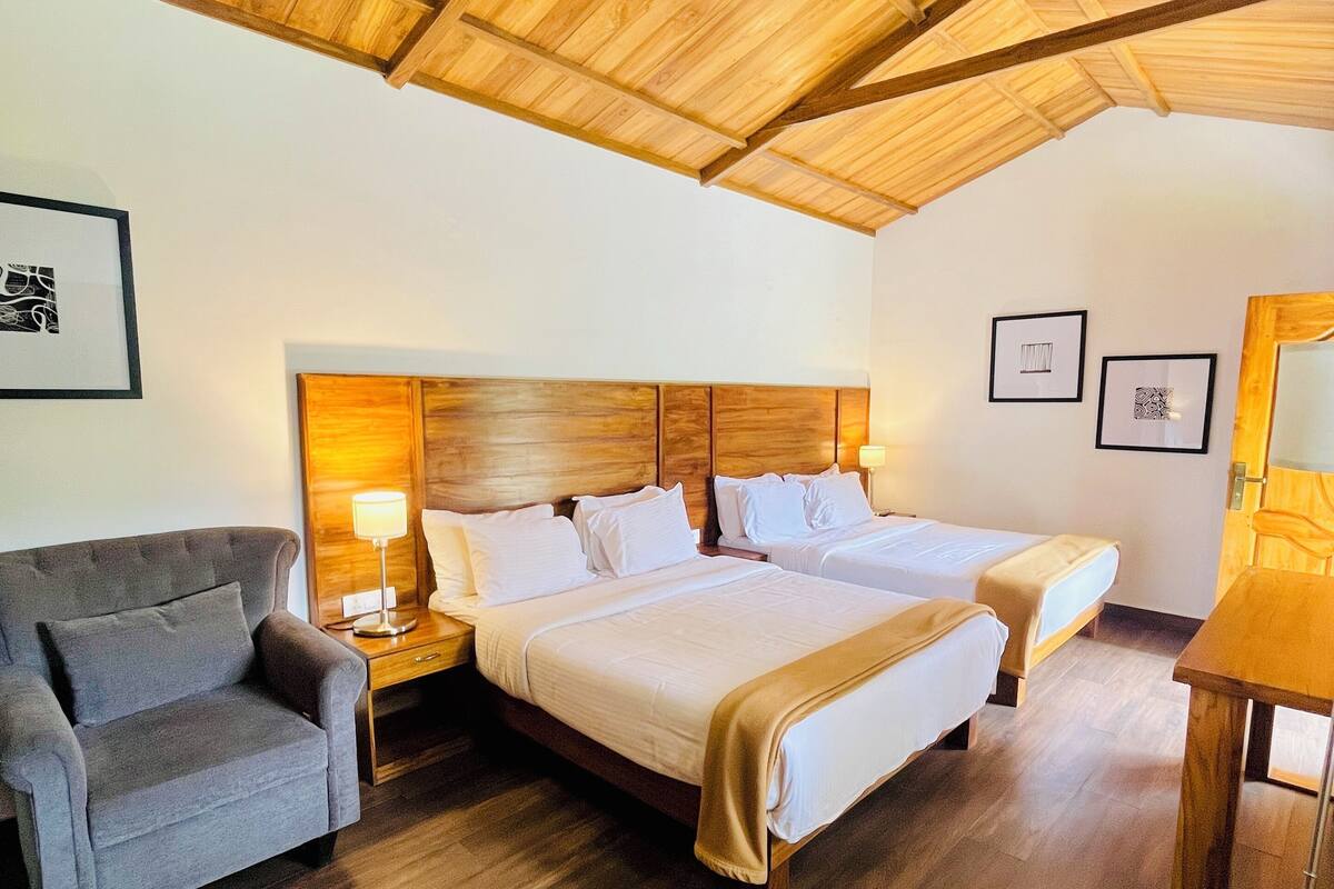 A room with a wooden ceiling, two beds, a sofa, and a table.