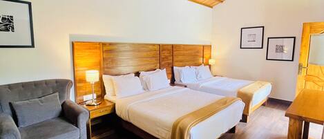 A room with a wooden ceiling, two beds, a sofa, and a table.