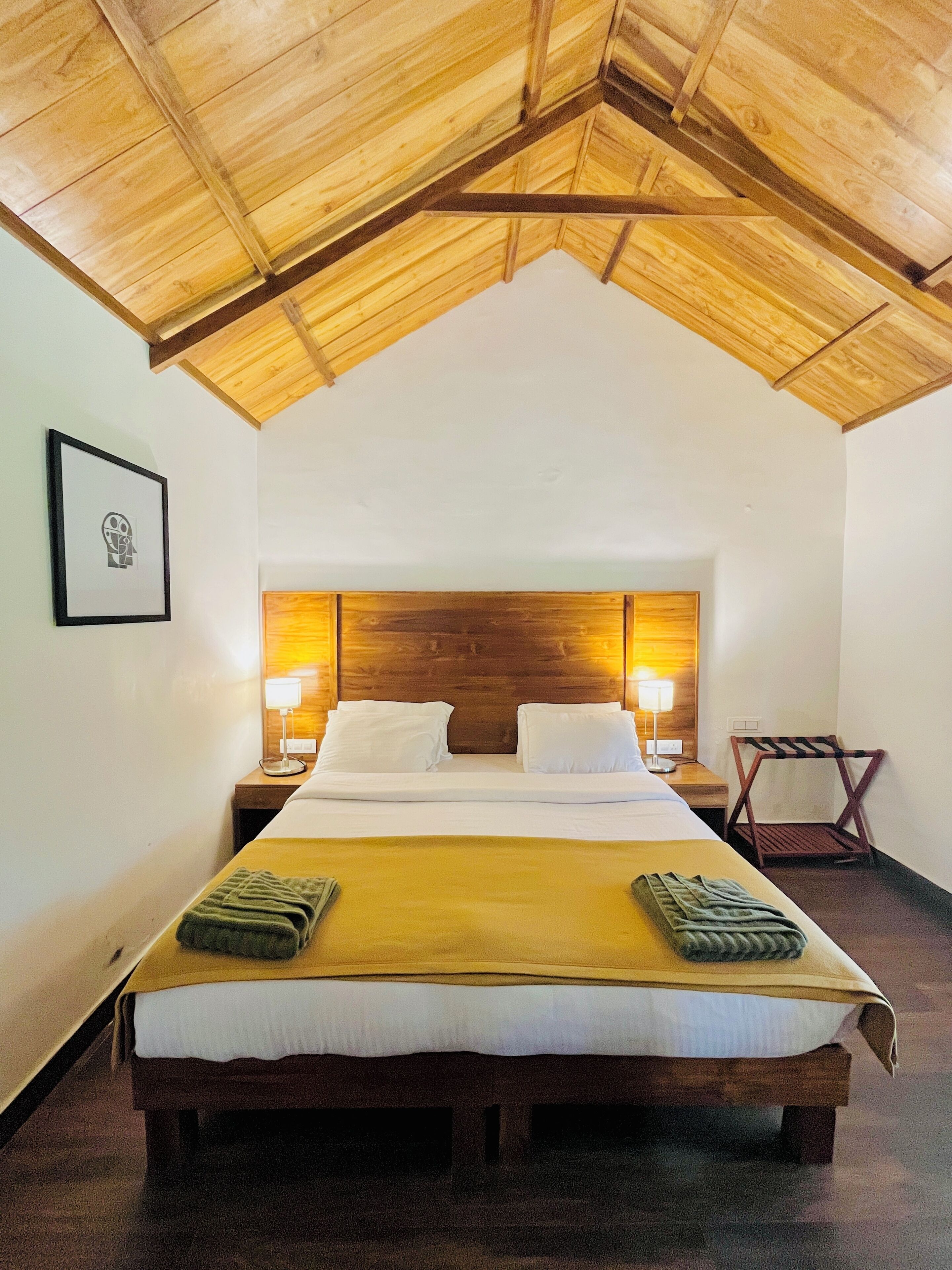 A single bed with a wooden headboard, two bedside lamps, a framed picture on the wall, and a wooden chair.