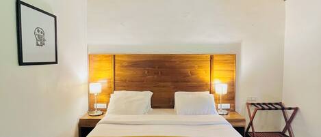 A single bed with a wooden headboard, two bedside lamps, a framed picture on the wall, and a wooden chair.