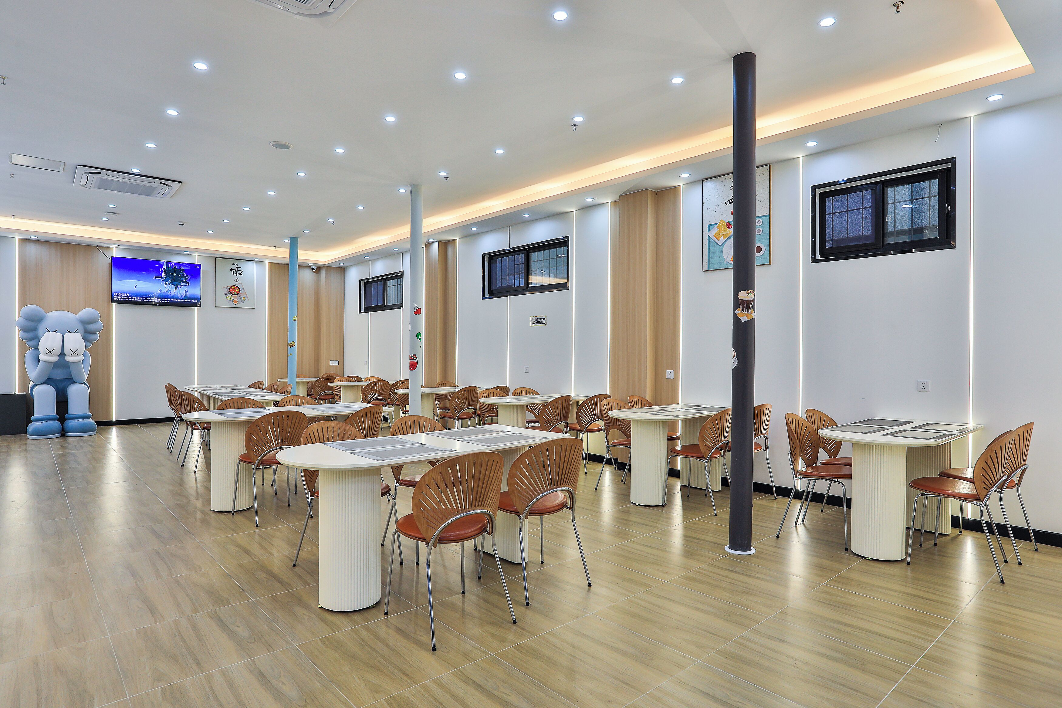 A spacious room with multiple tables and chairs, a large screen, and a unique sculpture.