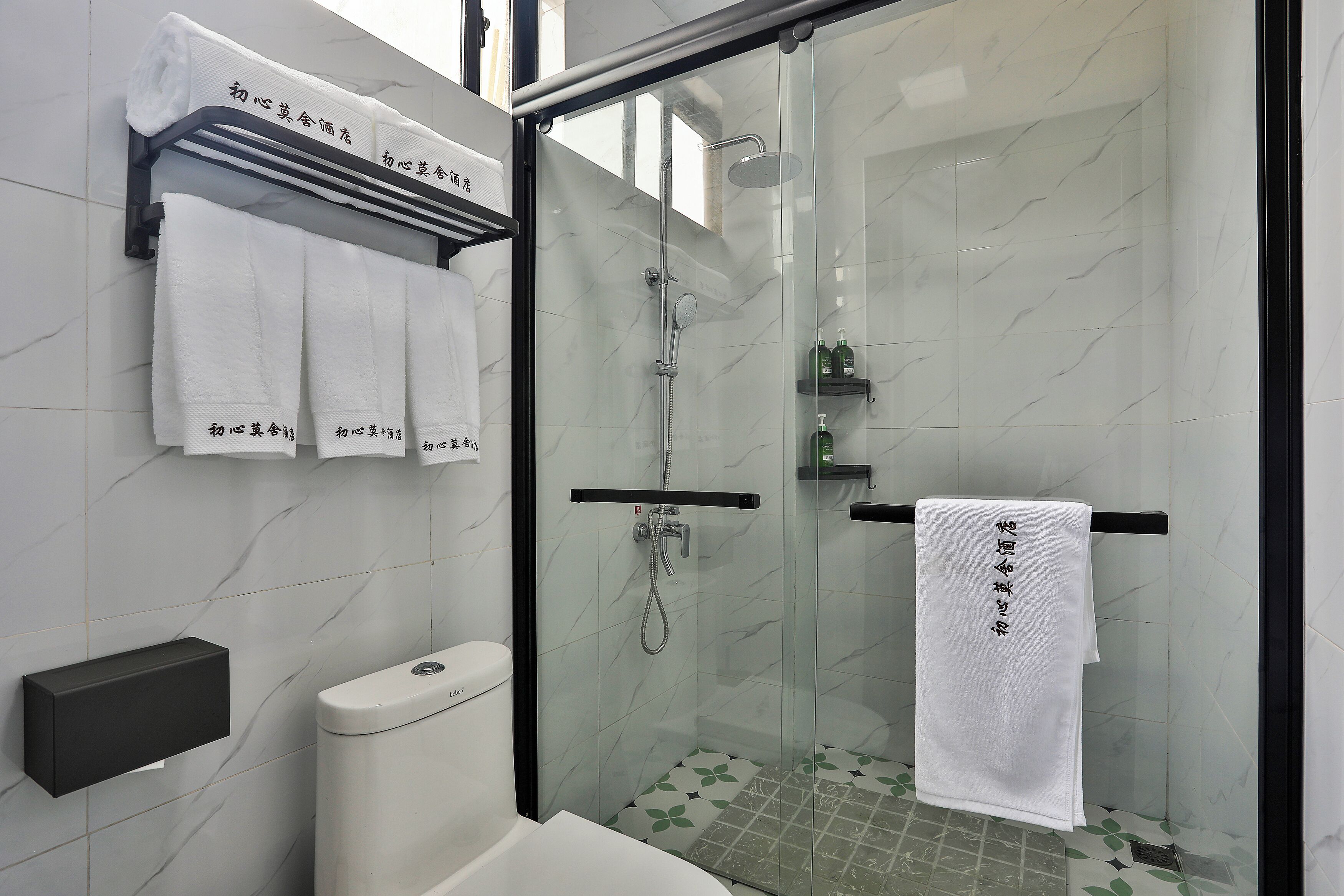 A modern bathroom with a glass-enclosed shower, a toilet, and a towel rack with multiple towels.