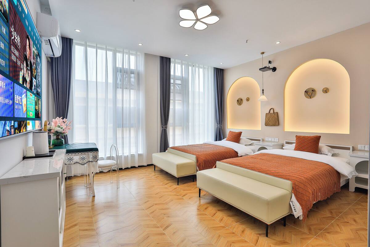 A modern hotel room with two beds, a desk, and a TV displaying a menu.
