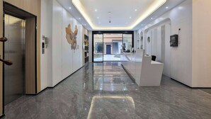 A modern hotel lobby with a reception desk, an elevator, and a glass door leading to the outside. - Chuxin Moshe Hotel (Shanghai)