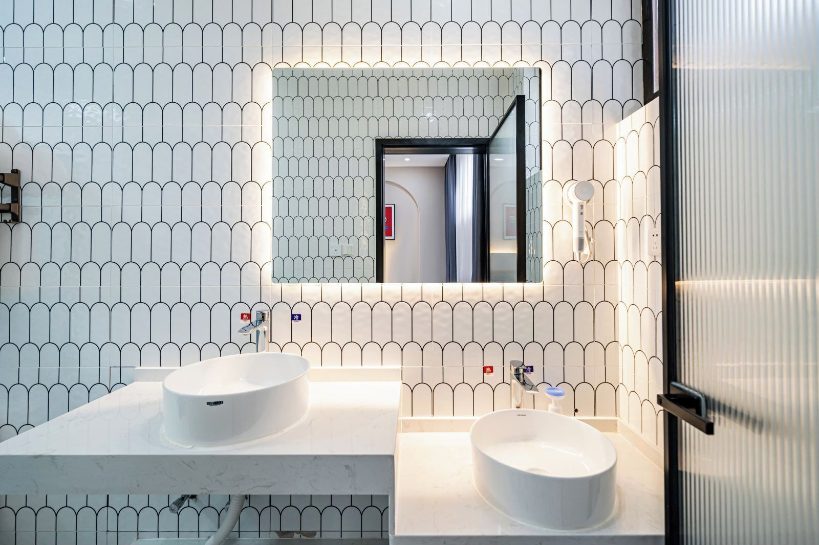 A modern bathroom with two sinks, a large mirror, and a patterned wall.