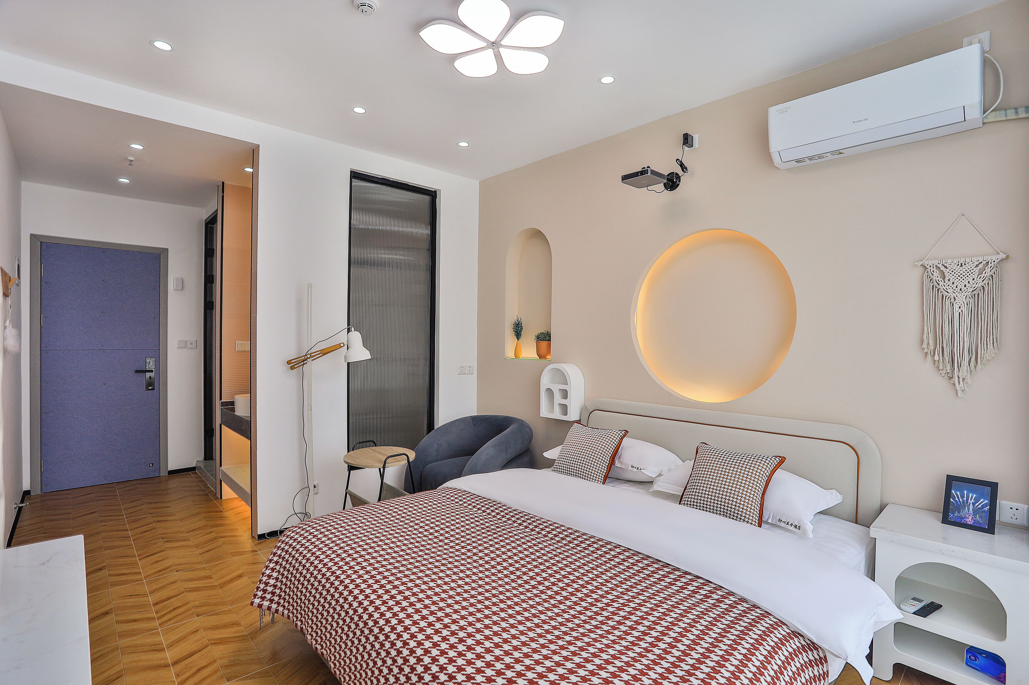A modern hotel room with a large bed, a desk, a chair, and a desk lamp.