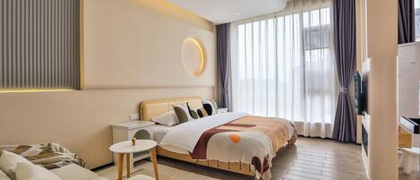Habitación de hotel moderna con una cama grande, zona de estar con sofá y sillón, una mesita y un televisor.