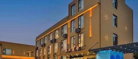 A multi-story hotel with a modern design, featuring a flat roof, large windows, and a covered outdoor area with seating.