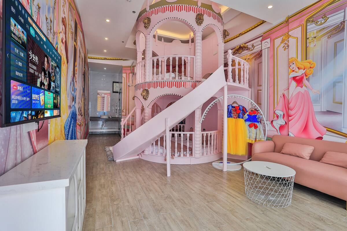 A children's play area with a pink spiral staircase, a slide, and a large cartoon character mural.