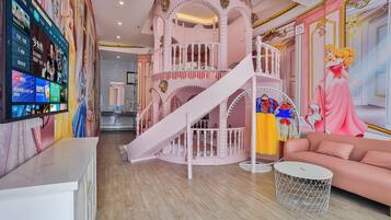 Un espace de jeux pour enfants avec un escalier en colimaçon rose, un toboggan et une grande fresque représentant un personnage de dessin animé.