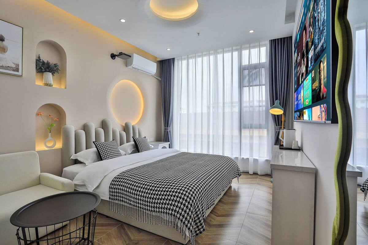 A modern hotel room with a large bed, a sofa, a small table, and a TV mounted on the wall.