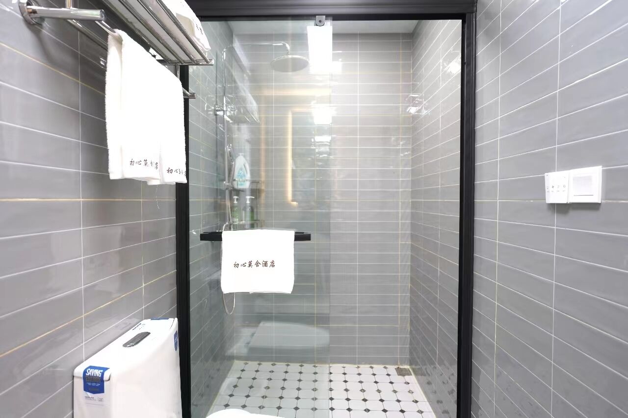 Ein kleines, modernes Badezimmer mit grauen Fliesen, einer Duschkabine aus Glas und einem weißen Handtuch an der Wand.