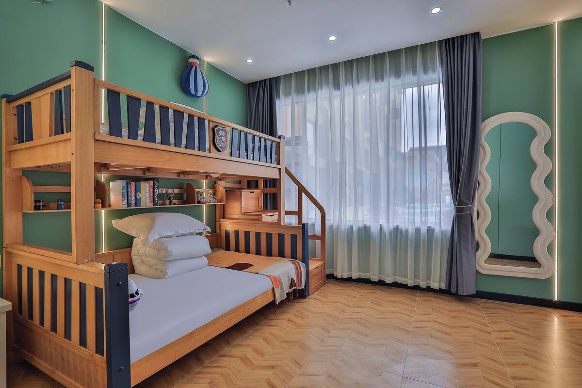 A bunk bed with a wooden frame, a small desk, and a bookshelf with books and a globe.