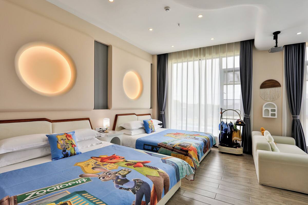 A hotel room with two beds, a sofa, a ceiling projector, and a window with curtains.