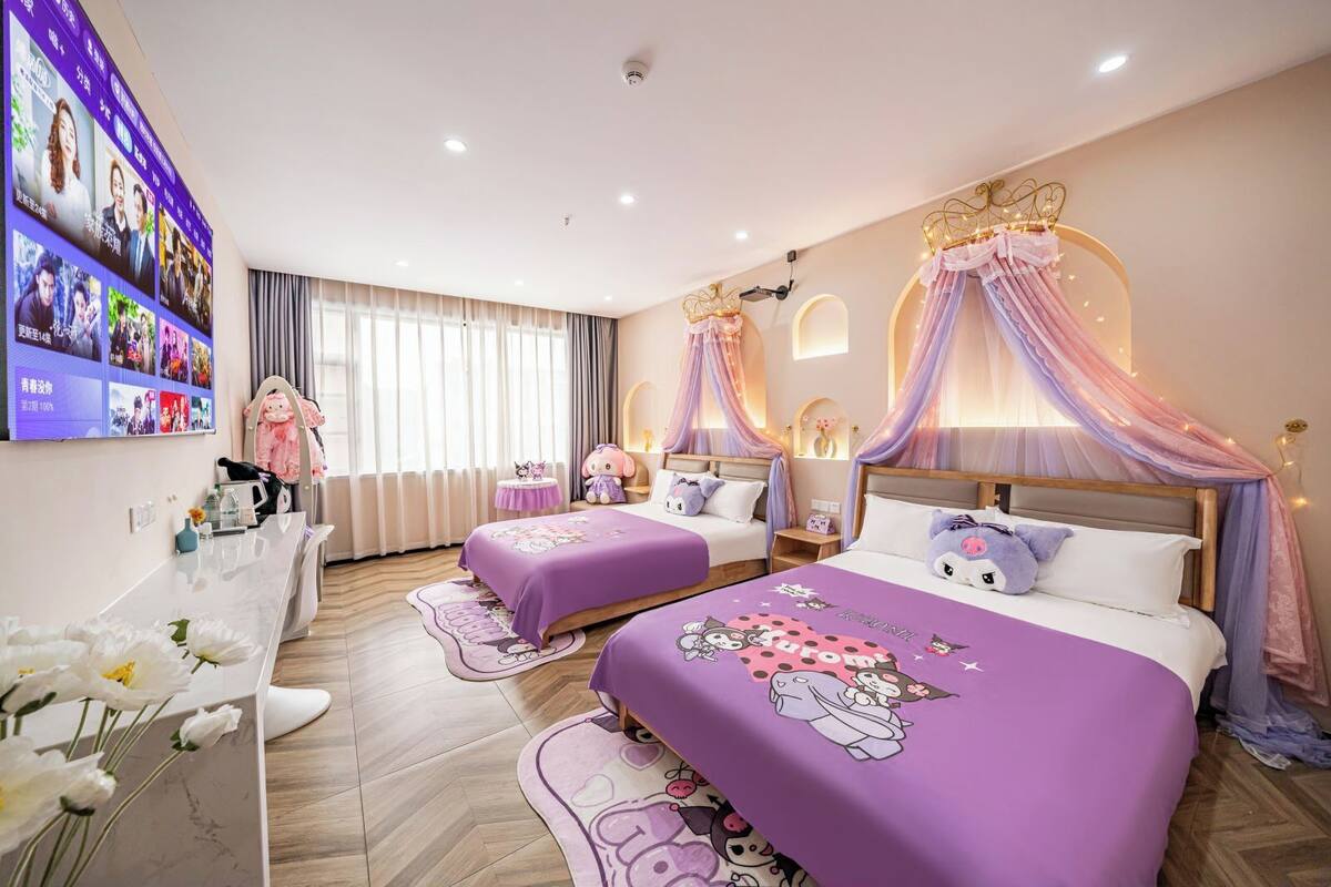 A bedroom with two beds, a vanity, and a TV mounted on the wall.